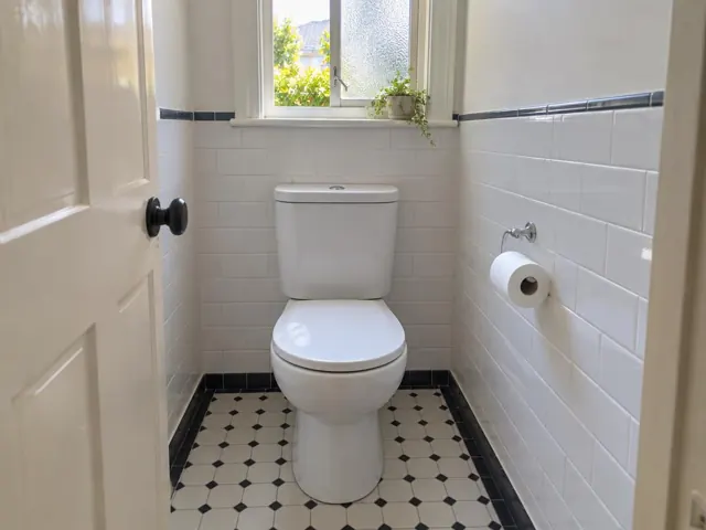 Clean white toilet in a tiled bathroom with a small window and patterned floor in Ryde