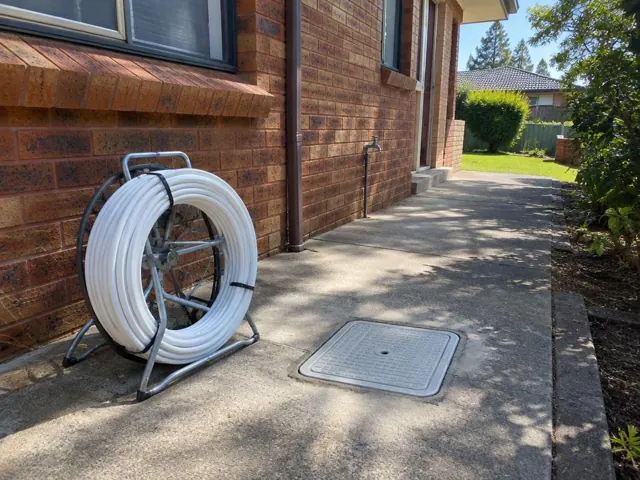 Concrete side path beside a brick house with a flush inspection cover and coiled pipe reel in Meadowbank