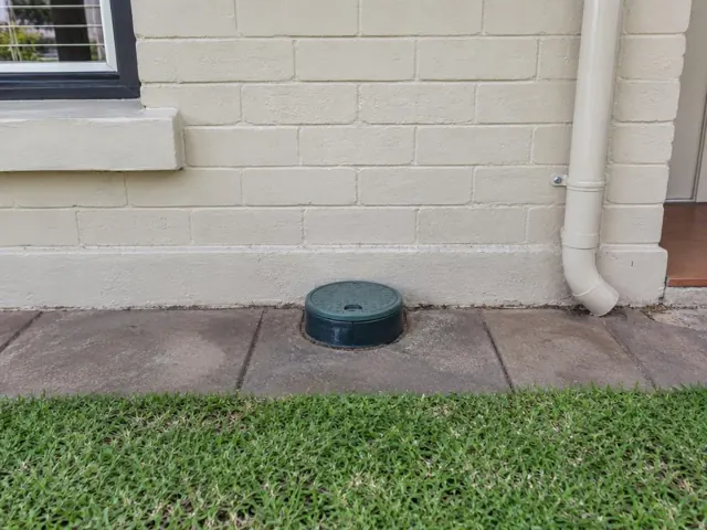 Capped sewer inspection opening beside a cream brick house and paved path in Ryde